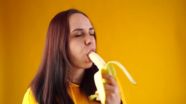 Κοντινό πλάνο της νεαρής γυναίκας τρώει μπανάνα σε κίτρινο φόντο. Ενηλίκων μελαχρινή απολαμβάνει νόστιμα φρούτα. — Αρχείο Βίντεο