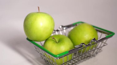 Yeşil elmaları beyaz arka plandaki küçük market arabasıyla kapat. Olgun meyve hasadı alıyorum. Süpermarkette organik gıda alışverişi kavramı.
