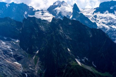 Bulutlu gökyüzüne karşı karlı dağ. Beyaz bulutların altından mavi gökyüzünde yüzen dağların üzerinden doğada güneşli bir günde karla kaplı..