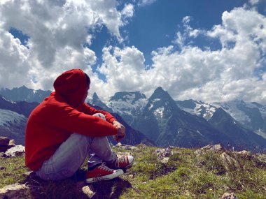 Genç adam bulutlu havada dağın zirvesinde oturuyor. Yetişkin adam dinleniyor, yazın muhteşem dağ manzarasının tadını çıkarıyor.