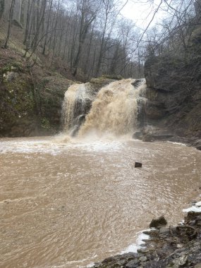 Dağlık arazide güzel, çamurlu bir şelale manzarası. Kirli dağ su yolu aşağı akıyor ve su sıçrıyor.