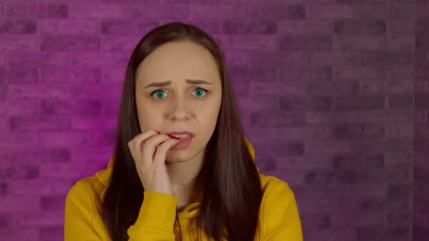 照明の壁を背景に若い女性が爪を噛むのを心配している 神経質な女の閉じるアップかむマニキュア — ストック動画