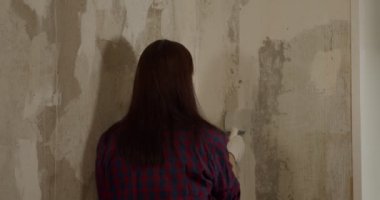 Eldivenli, spatulası olan, duvarları düzleştiren bir kadın. Genç bir kadın duvarları zımparalıyor ve dairede resim yapmaya hazırlanıyor. Tamir işi kavramı.
