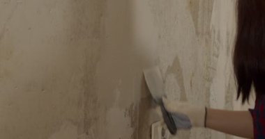 Odadaki duvara macun yapıştıran eldivenli genç bir kadın. Dişi sıva duvar macun bıçağıyla kaplanmış ve dairede resim yapmaya hazırlanıyor. Tamir işi kavramı.