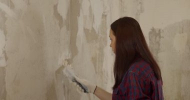 Odadaki duvara macun yapıştıran eldivenli genç bir kadın. Dişi sıva duvar macun bıçağıyla kaplanmış ve dairede resim yapmaya hazırlanıyor. Tamir işi kavramı.