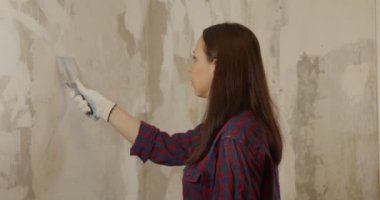 Eldivenli, spatulası olan, duvarları düzleştiren bir kadın. Genç bir kadın duvarları zımparalıyor ve dairede resim yapmaya hazırlanıyor. Tamir işi kavramı.