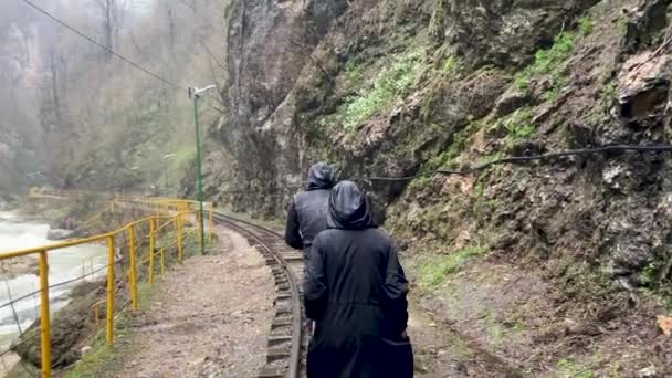 山岳地帯で鉄道を歩く観光客のリアビュー 雨と曇りの日に鉄道で男と女のハイキング — ストック動画