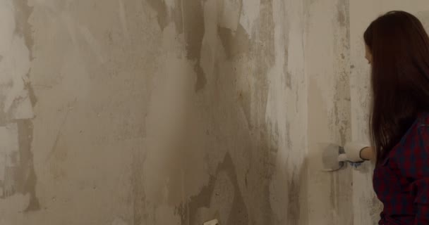 Gros plan de la jeune femme avec des gants appliquant du mastic sur le mur dans la chambre. Mur de plâtrage féminin avec couteau à mastic et préparation à la peinture dans l'appartement. Concept de travaux de réparation. — Video
