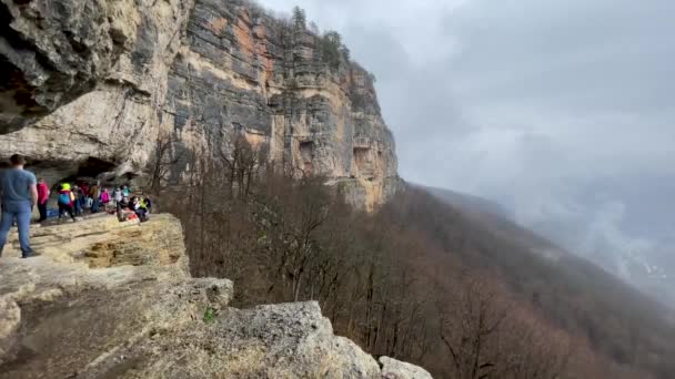 自然の壮大な景色と巨大な崖の上の観光客 霧と曇天の中 高い岩の上の人々のグループ — ストック動画