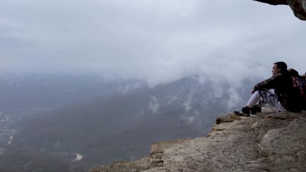 自然の壮大な景色と巨大な崖の上の観光客 霧と曇天の中 高い岩の上の人々のグループ — ストック動画