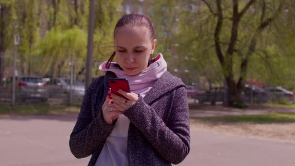 Close-up van jonge vrouw met mobiele telefoon op straat bij zonnig weer. Portret van vrouwelijke browsen smartphone en staan op frisse lucht. — Stockvideo