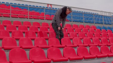 Stadyum tribünlerinde tek başına oturan genç adam. Spor stadyumunda üzgün yetişkin bir erkek. Kamu etkinlikleri ve yarışmalara kısıtlamalar.