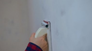 Duvarı zımpara kağıdıyla boyayan genç bir kadının yan görüntüsü. Dairenin duvarını boyayan bir kadın. Tamir işleri ve konut koşullarının iyileştirilmesi.