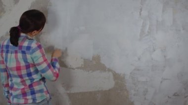 Odanın duvarına macun yapıştıran tanınmayan birinin arka görüntüsü. Dairesinde spatulayla duvarları sıvayan kimliği belirsiz bir kadın. Tamir işleri ve konut koşullarının iyileştirilmesi.