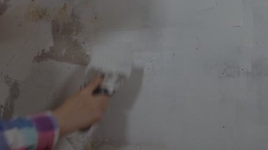 Odanın duvarına macun yapıştıran tanınmayan kişiye yakın çekim. Dairesinde spatulayla duvarları sıvayan kimliği belirsiz bir kadın. Tamir işleri ve konut koşullarının iyileştirilmesi.