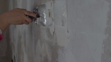 Odanın duvarına macun yapıştıran tanınmayan kişiye yakın çekim. Dairesinde spatulayla duvarları sıvayan kimliği belirsiz bir kadın. Tamir işleri ve konut koşullarının iyileştirilmesi.