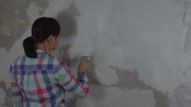 Odanın duvarına macun yapıştıran tanınmayan birinin arka görüntüsü. Dairesinde spatulayla duvarları sıvayan kimliği belirsiz bir kadın. Tamir işleri ve konut koşullarının iyileştirilmesi