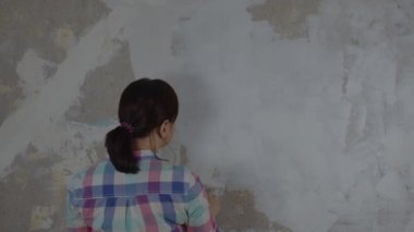 Odanın duvarına macun yapıştıran tanınmayan birinin arka görüntüsü. Dairesinde spatulayla duvarları sıvayan kimliği belirsiz bir kadın. Tamir işleri ve konut koşullarının iyileştirilmesi