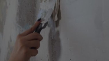Odanın duvarına macun yapıştıran tanınmayan kişiye yakın çekim. Dairesinde spatulayla duvarları sıvayan kimliği belirsiz bir kadın. Tamir işleri ve konut koşullarının iyileştirilmesi.