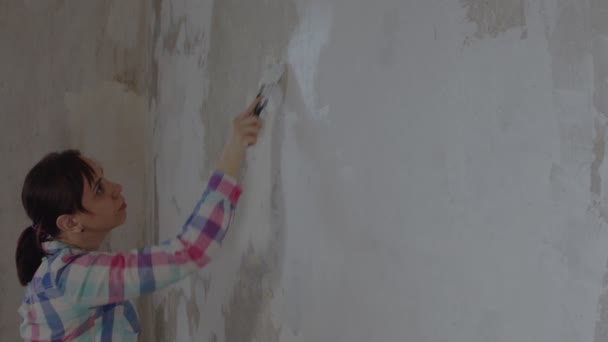 部屋の壁にパテを適用する若い女性の側面図 アパートのへらで壁を漆喰女性労働者 補修工事の概念及び住宅条件の改善 — ストック動画