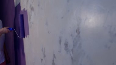 Kadının elini koruyucu eldivenle kapat. Duvarı mor renklerle boyarsın. Duvara boya sürerken tanınmayan biri. Tamir işleri ve konut koşullarının iyileştirilmesi.