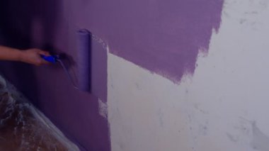 Kadının elini koruyucu eldivenle kapat. Duvarı mor renklerle boyarsın. Duvara boya sürerken tanınmayan biri. Tamir işleri ve konut koşullarının iyileştirilmesi