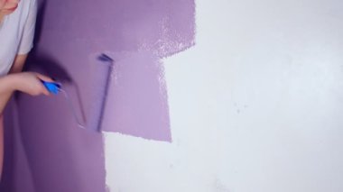 Kadının elini koruyucu eldivenle kapat. Duvarı mor renklerle boyarsın. Duvara boya sürerken tanınmayan biri. Tamir işleri ve konut koşullarının iyileştirilmesi
