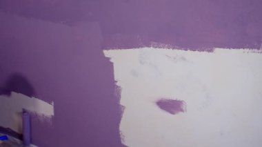 Kadının elini koruyucu eldivenle kapat. Duvarı mor renklerle boyarsın. Duvara boya sürerken tanınmayan biri. Tamir işleri ve konut koşullarının iyileştirilmesi.