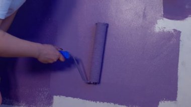 Kadının elini koruyucu eldivenle kapat. Duvarı mor renklerle boyarsın. Duvara boya sürerken tanınmayan biri. Tamir işleri ve konut koşullarının iyileştirilmesi