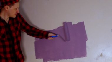 Dans eden ve duvarları mor renkte silindirle boyayan genç adama yaklaş. Duvara boya süren mutlu erkek.. 