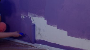 Kadının elini koruyucu eldivenle kapat. Duvarı mor renklerle boyarsın. Duvara boya sürerken tanınmayan biri. Tamir işleri ve konut koşullarının iyileştirilmesi