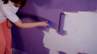 Kadının elini koruyucu eldivenle kapat. Duvarı mor renklerle boyarsın. Duvara boya sürerken tanınmayan biri. Tamir işleri ve konut koşullarının iyileştirilmesi