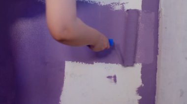 Kadının elini koruyucu eldivenle kapat. Duvarı mor renklerle boyarsın. Duvara boya sürerken tanınmayan biri. Tamir işleri ve konut koşullarının iyileştirilmesi