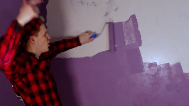 Dans eden ve duvarları mor renkte silindirle boyayan genç adama yaklaş. Duvara boya süren mutlu erkek.. 