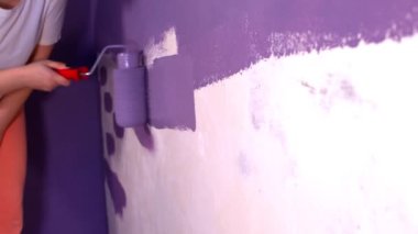 Kadının elini koruyucu eldivenle kapat. Duvarı mor renklerle boyarsın. Duvara boya sürerken tanınmayan biri. Tamir işleri ve konut koşullarının iyileştirilmesi.