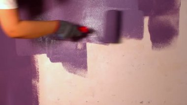 Kadının elini koruyucu eldivenle kapat. Duvarı mor renklerle boyarsın. Duvara boya sürerken tanınmayan biri. Tamir işleri ve konut koşullarının iyileştirilmesi