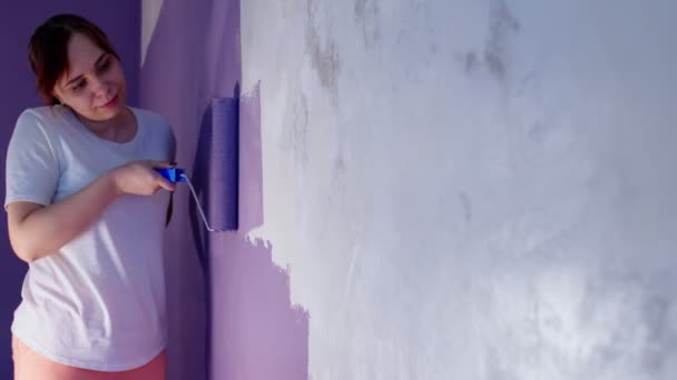 用胶辊把年轻女子漆成紫色的墙关上 女设计师在墙上涂漆 维修工作的概念和改善住房条件 — 图库视频影像