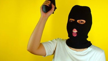 Siyah kar maskeli, sarı arka planda silahı olan tanınmamış bir kadın. Maskeli tehlikeli kadın kameraya nişan alıyor, ateş ediyor ve gülüyor. Yavaş çekim.