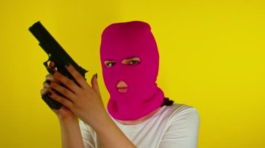Sarı arka planda silahlı, pembe kar maskeli tanınmayan bir kadın. Maskeli tehlikeli kadın kameraya nişan alıp ateş ediyor. Yavaş çekim