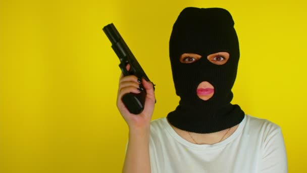 无法辨认的女人穿着黑色巴拉克拉瓦 枪托在黄色背景上 戴面具的危险女性瞄准镜头 镜头和笑声 慢动作 — 图库视频影像