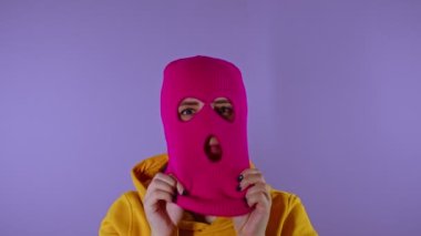 Yakın plan genç bayan mor arka planda pembe kar maskesi takıyor. Gizemli kadın maskeyi takar ve kameraya bakar..