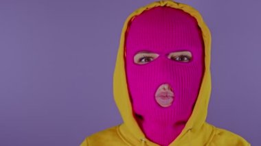 Pembe kar maskeli tanınmayan bir kadın mor arka planda öpücük yolluyor. Kimliği belirsiz kadın kameraya bakıyor ve öpücüklerle ördek suratı yapıyor..