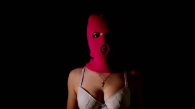 Pembe kar maskeli ve beyaz sütyenli tanınmayan bir kadın karanlıkta duruyor. Karanlık odada maskeli ve iç çamaşırlı bilinmeyen bir kadın var..