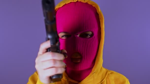 无法辨认的女人穿着粉红色的巴拉克拉瓦带着紫色背景的枪戴面具的危险女性瞄准镜头 镜头和笑声 慢动作 — 图库视频影像