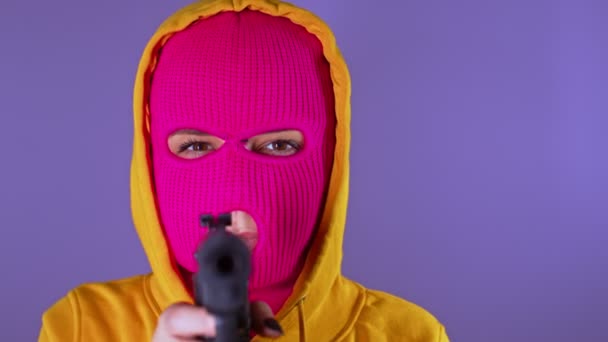 无法辨认的女人穿着粉红色的巴拉克拉瓦带着紫色背景的枪戴面具的危险女性瞄准相机和射击 慢动作 — 图库视频影像