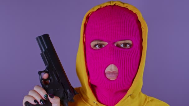 无法辨认的女人穿着粉红色的巴拉克拉瓦带着紫色背景的枪戴面具拿着手枪看着摄像机的危险罪犯 — 图库视频影像