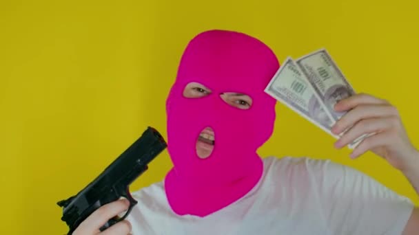 穿着粉色巴拉克拉瓦的男子的近身镜头 背景是黄色的金钱和枪枝 不知名的家伙跳舞与美元和手枪 盗窃和抢劫的概念 — 图库视频影像