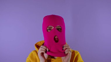 Yakın plan genç bayan mor arka planda pembe kar maskesi takıyor. Gizemli kadın maskeyi takar ve kameraya bakar.
