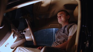 Direksiyonun başında oturan ve gece gözünü kaçıran genç adama yaklaş. Yorgun adam araba kullanmaktan ve düşünceli bakışlardan arabasında dinleniyor.