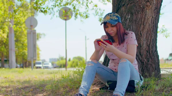 여자는 길에서 근처에 핸드폰을 있습니다 스마트폰 모자를 브루넷은 여름에 근처에서 — 스톡 사진